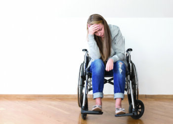 Jeune femme assise sur un fauteuil roulant et se tenant la tête. SED