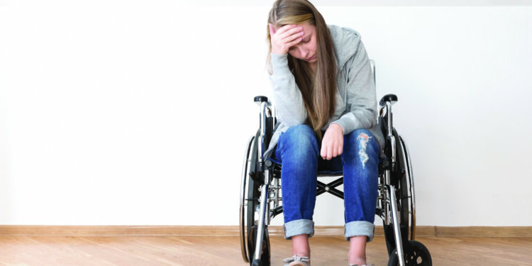 Jeune femme assise sur un fauteuil roulant et se tenant la tête. SED