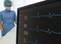 Écran de surveillance médicale affichant le rythme cardiaque, la température corporelle et la saturation en oxygène, avec une infirmière en arrière-plan