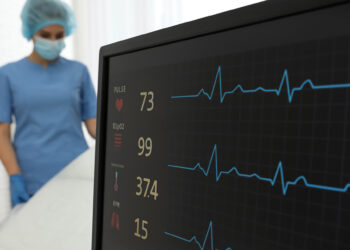 Écran de surveillance médicale affichant le rythme cardiaque, la température corporelle et la saturation en oxygène, avec une infirmière en arrière-plan