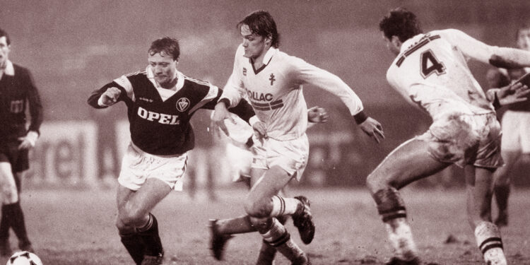 Sylvain Kastendeuch face à Bernard Lacombe lors d’un match des années 1980, sous la pluie, dans un duel serré au milieu du terrain.